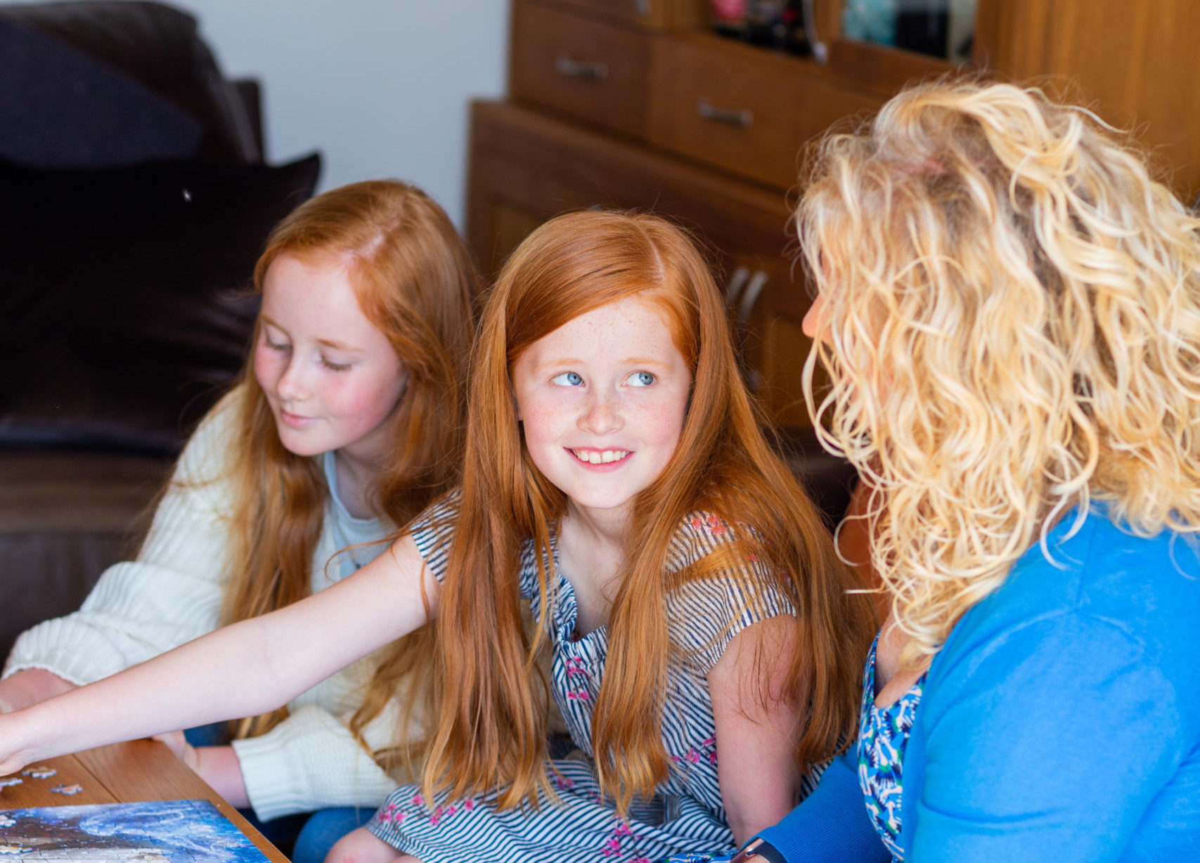 Two little girls and an adult woman are working on a puzzle